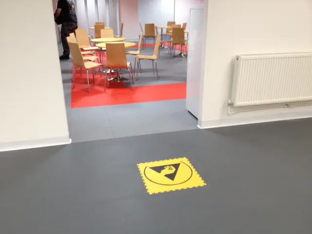 A room with a yellow floor and chairs in the background.