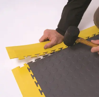 A person cutting a piece of yellow and gray floor.